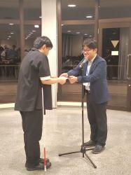 イブニングセッションでのショートビデオ受賞式にて、大会長の中澤先生（右）から賞状を受け取る川本さん（左）の写真